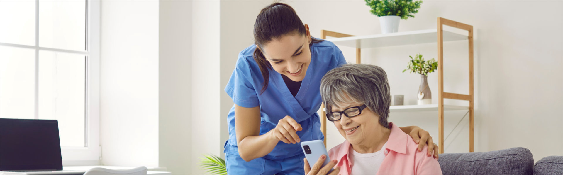 Smiling caregiver and senior woman in nursing home looking at mobile phone screen together
